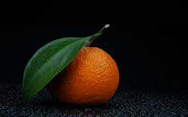 Wall Mural - Ripe juicy tangerine on a black background with water drops.