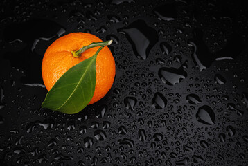 Wall Mural - Ripe juicy tangerine on a black background with water drops.