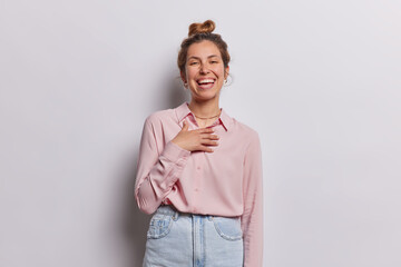 Wall Mural - People and happiness. Studio photo of young fit pretty cheerful smiling broadly European lady standing in centre isolated on white background wearing pink blouse and blue jeans keeping hair in bun