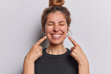 Photo Of Pleasant Looking Cheerful Woman Points Index Fingers At Toothy Smile Shows Wwell Cared Whie Even Teeth Dressed In Casual Black T Shirt Isolated Over Whtie Studio Background Feels Happy