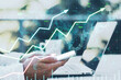 Close up of male hands using laptop and cellphone at desk with coffee cup and growing upward chart, map, arrows and forex graph on blurry background. Trading and finance concept. Double exposure.