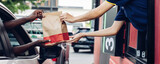 Fototapeta  - Hand Man in car receiving coffee in drive thru fast food restaurant. Staff serving takeaway order for driver in delivery window. Drive through and takeaway for buy fast food for protect covid19.