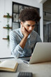 © Anatoliy Karlyuk - Upset tired exhausted african american male student studying online sitting at table using laptop, finishing his thesis, making last corrections and edits. Remote education concept