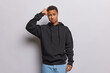 Photo of confused hesitant dark skinned African man scratching head while being puzzled or clueless feels doubtful dressed in casual black sweatshirt and jeans isolated over white background.