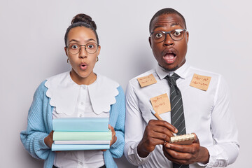 Teaching and learning concept. Indoor photo of young surprised African american man and woman wearing smart clothes holding books notebook pen standing in centre isolated on white background