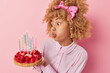 © WHstudio Leushin N - People and celebration. Indoor sideway photo of young pretty African american female having party standing in centre isolated on pink background holding cake with strawberries blowing candles