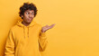 Confused hesitant Hindu man shrugs shoulder keeps palm raised up dressed in casual sweatshirt doesnt know why happened like this isolated over yellow background copy space for your promotion