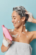 © wayhome.studio  - Asian woman basks in the pleasure of her invigorating shower with eyes closed and serene smile she applies shampoo to her luscious hair wrapped in bath towel isolated over blue wall. Hygiene concept