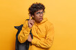 Studio waist up of young Hindu male student standing in centre isolated on yellow background wearing hoodie with black bag on left shoulder using hand gesture wanting to grab attention and warn you