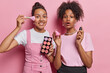 Two women spend time at home together having fun putting make up on hold palette foundation look surprisingly dressed in stylish clothes isolated over pink background preparing for special occasion