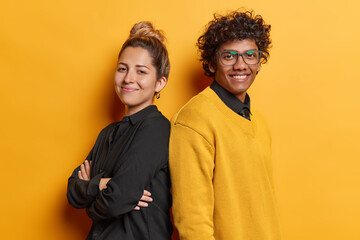Photo of cheerful woman and man stand backs with folded arms feel happy and self confident dressed in casual clothing smile satisfied isolated on yellow background. Friendly team collaborate together