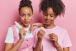 Beauty concept. Studio shot of two pretty young happy satisfied African american women standing isolated close to each other in centre on pink background wearing casual clothes holding nail files