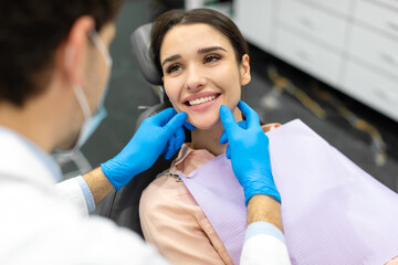 Male dentist checking teeth of an attractive woman, doctor in rubber gloves touches the patient's teeth during checkup