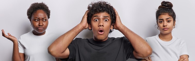 Wall Mural - Photo of shocked curly haired Hindu man stares with disbelief displeased African woman keeps palm raised up being dissatisfied Iranian girl keeps arms folded isolated over white studio background