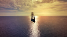Aerial Drone Photo Of Beautiful Three Mast Barque Or Barc Type Classic Sailing Wooden Boat With Huge Waving Flag Anchored In Mediterranean Deep Blue Aegean Sea At Sunset With Golden Colours