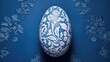  a blue and white painted egg sitting on top of a blue and white flowered tablecloth covered tablecloth.