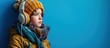preteen child in ear muffs and scarf standing in winter outfit on turquoise backdrop pouting lips. Creative Banner. Copyspace image