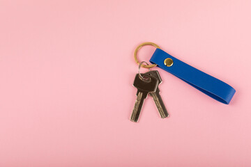 Leather keychain with a key ring on a pink background. Concepts for real estate and moving home or renting property. Buying a property. Mock-up keychain.Copy space.