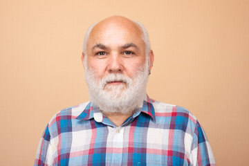 Face of 60s elderly retired mature aged pensioner. Portrait of an mature senior man with grey beard isolated on beige studio background.