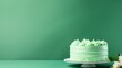  a green frosted cake sitting on top of a white plate next to a white flower on a green table.