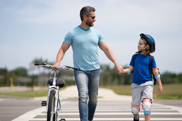 Wall Mural - Kids insurance. Safety on road. Pedestrian crossing for cyclists. Happy playful dad with excited kid son riding a bicycle on weekend. Sporty family. Fathers day. Father teaching and support child.