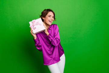 Sticker - Photo of smiling beautiful young brown bob hair lady hold pink surprise package at birthday holiday isolated on green color background