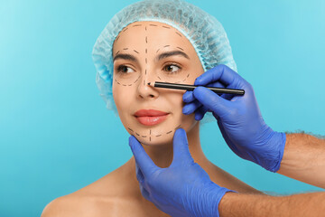 Wall Mural - Doctor with pencil preparing patient for cosmetic surgery operation on light blue background, closeup