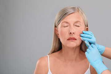 Sticker - Doctor giving facial injection to senior woman on light grey background, closeup and space for text. Cosmetic surgery