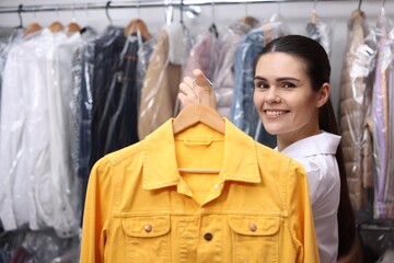 Wall Mural - Dry-cleaning service. Happy worker holding hanger with jacket indoors