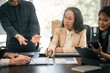 © makibestphoto - diverse group of Asian professionals, including middle-aged and mature individuals, gathered around a table in a business setting, discussing documents with focused attention.