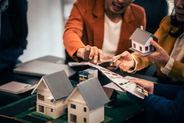 Asian real estate team engaged in a discussion, with two men and a woman focusing on a house model on a table, suggesting a planning or sales meeting.