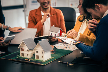 Wall Mural - Asian real estate team engaged in a discussion, with two men and a woman focusing on a house model on a table, suggesting a planning or sales meeting.