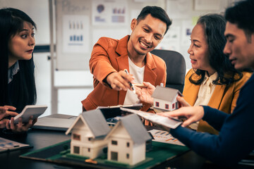 Wall Mural - Asian real estate team engaged in a discussion, with two men and a woman focusing on a house model on a table, suggesting a planning or sales meeting.