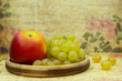 Still life of apple and grapes on a vintage background. Poster for interior. Fruits on a wooden plate close-up.