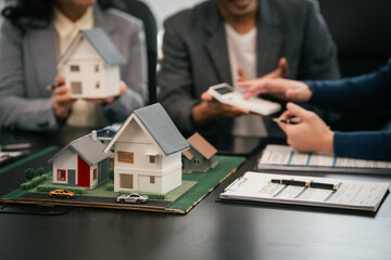 Wall Mural - Asian real estate team engaged in a discussion, with two men and a woman focusing on a house model on a table, suggesting a planning or sales meeting.