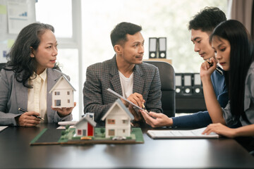 Wall Mural - Asian real estate team engaged in a discussion, with two men and a woman focusing on a house model on a table, suggesting a planning or sales meeting.