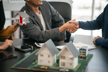 Wall Mural - Asian real estate agent team engaged in a discussion, with two men and a woman focusing on a house model on a table, suggesting a planning or sales meeting.