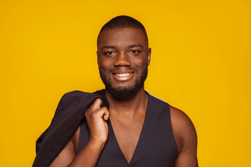 Happy young african american stylish attractive man wears suit vest showing torso at studio isolated over yellow background. Stylish male, fashion concept.