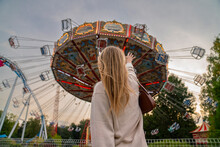 Blond Woman Reaching Towards Carousel In Amusement Park At Sunset
