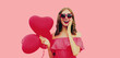 Sweet portrait of happy surprised young woman holding pink heart shaped balloon on isolated on studio background