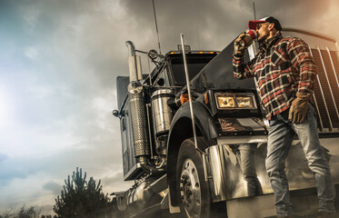 Wall Mural - Caucasian Driver Drinking Hot Coffee in Front or His Semi Truck Tractor