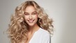 © Elchin Abilov - A young woman's smiling face is surrounded by beautifully groomed, curly, long, deep blonde hair.