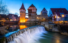 Panoramic View Of Historic Buidings, Castle And Cascade Of Eyach River In Old Town In Balningen (Baden-Wuerttemberg, Germany). Half Timbered And Illuminated Facades At Evening Twilight In Winter.
