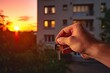 © Fedash - Real estate concept. A man's hand holds the keys to a new apartment or house. Against the background of the building. Close-up. Blurred background.
