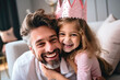 © Katerina Bond - Father with cute birthday hat playing with little girl with toy crown, white home living room, childhood, positive and happiness.
