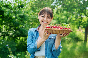 Wall Mural - Happy woman with harvest of red ripe cherries in summer garden