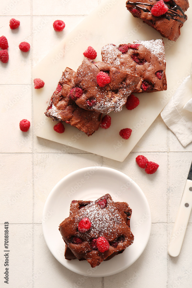 Board and plate with pieces of raspberry chocolate brownie on white tile background