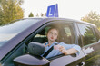 © Iryna - Young beautiful woman successfully passed driving school test. Female smiling and holding driver's license in a brown car with blue L plate on a roof.