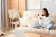 © Pixel-Shot - Young woman in warm sweater sitting on sofa at home