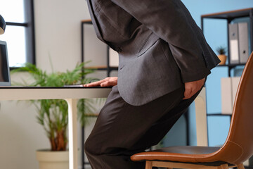 Poster - Young businessman with hemorrhoids sitting on chair in office